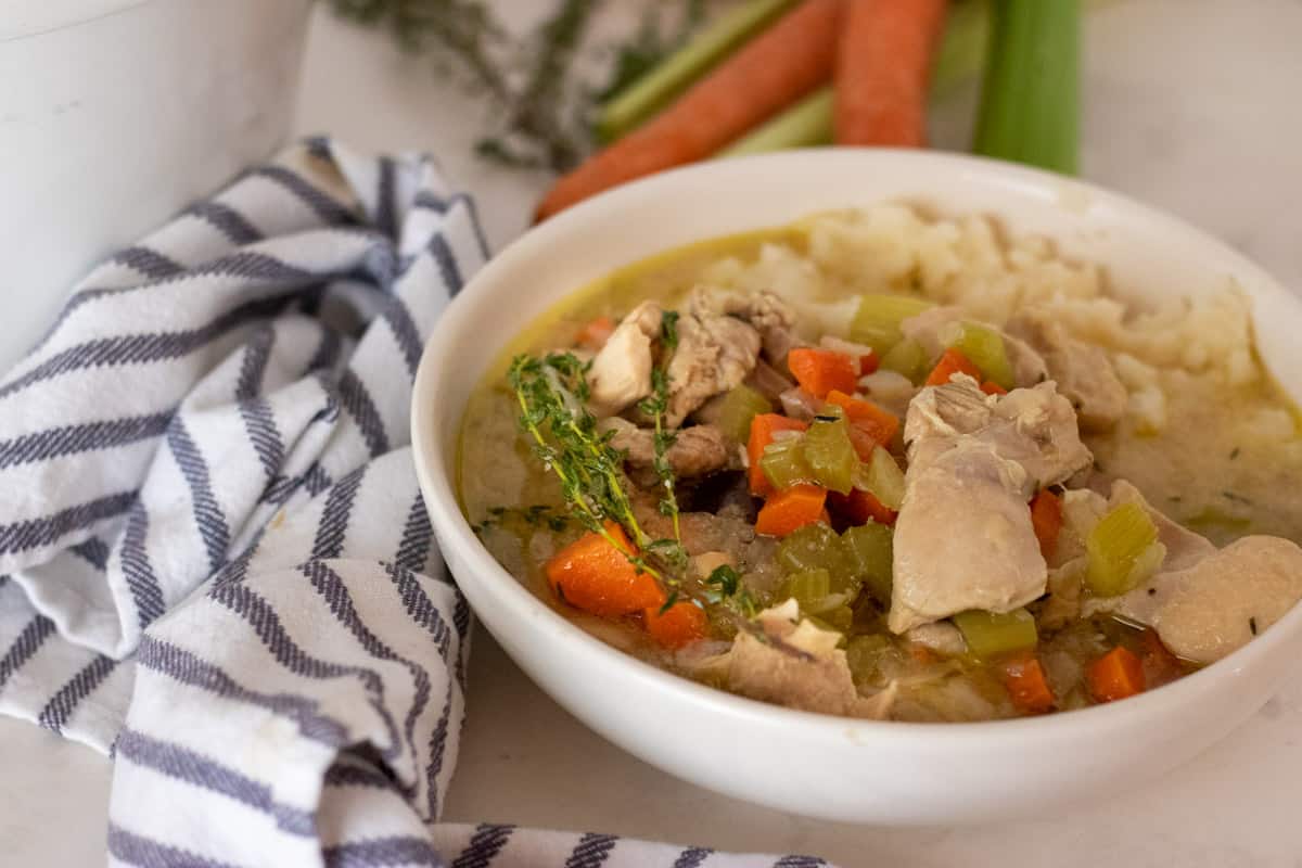 Chicken stew in a white bowl with a blue and white striped napkin.