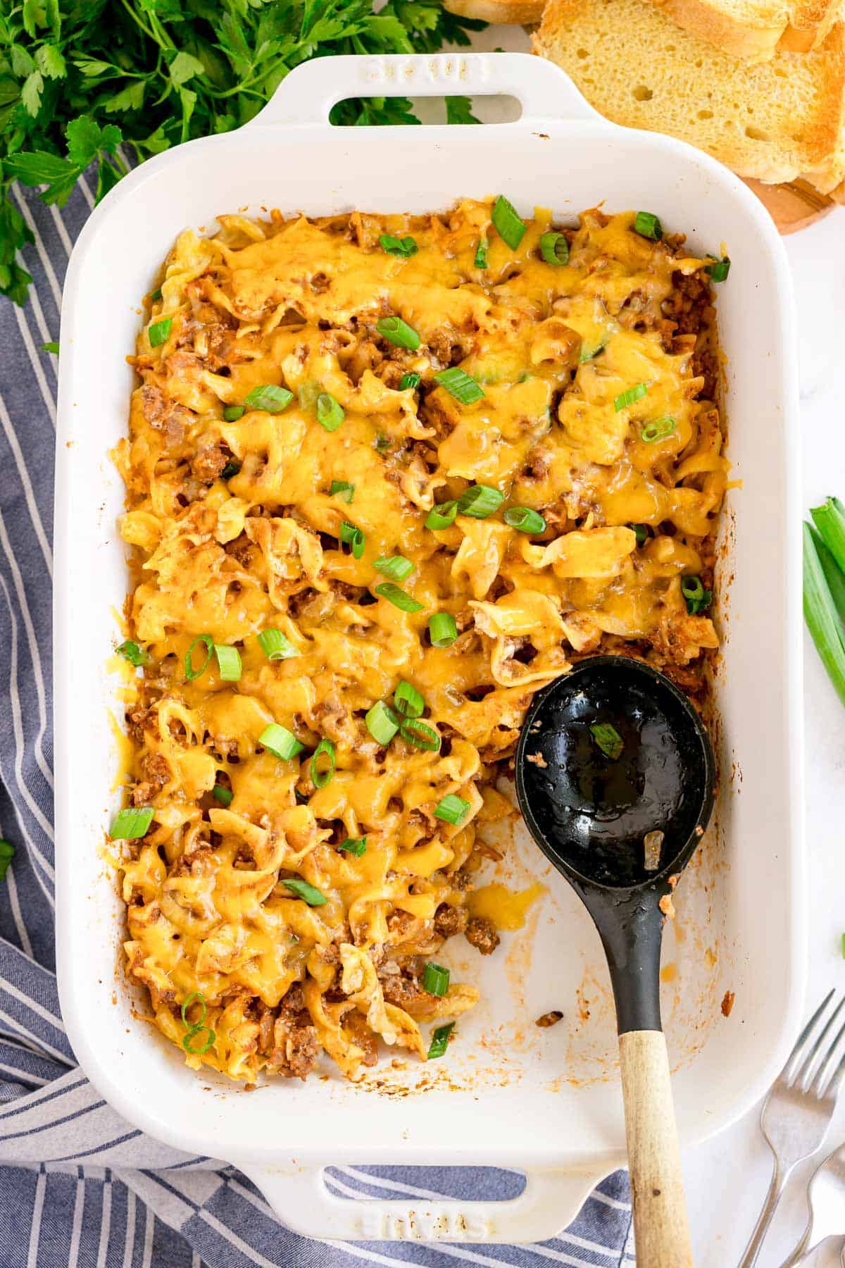A casserole dish of baked sour cream noodle bake with a spoon inside and part of the dish served.