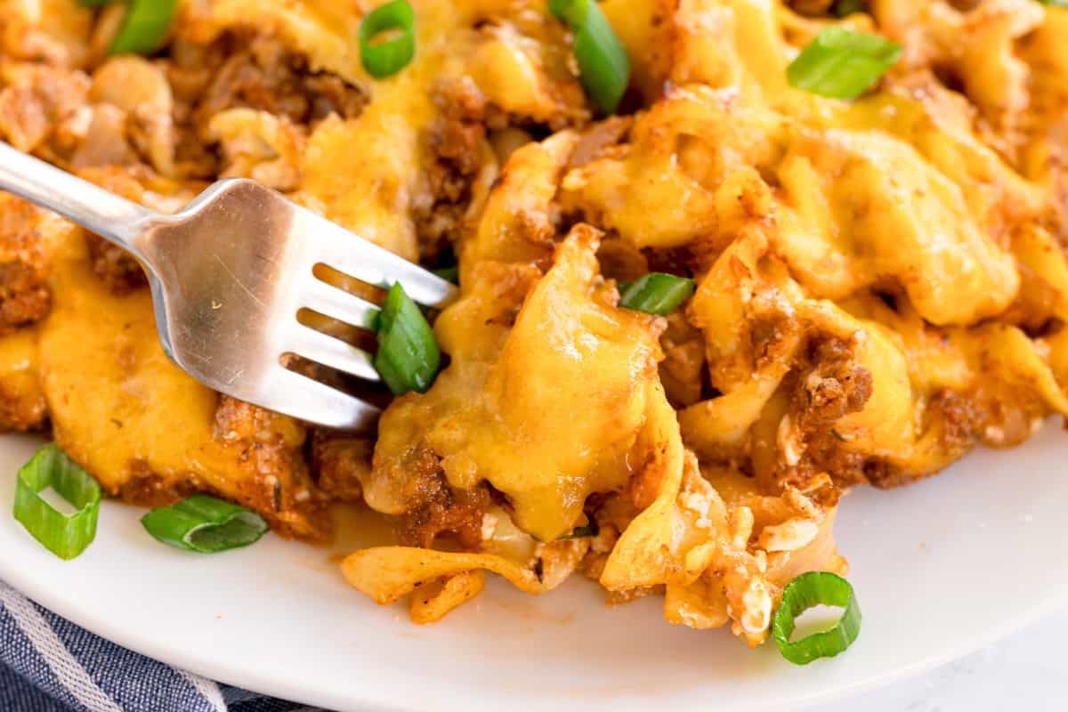 A fork resting on a plate of cheesy beef noodle bake, garnished with green onions.