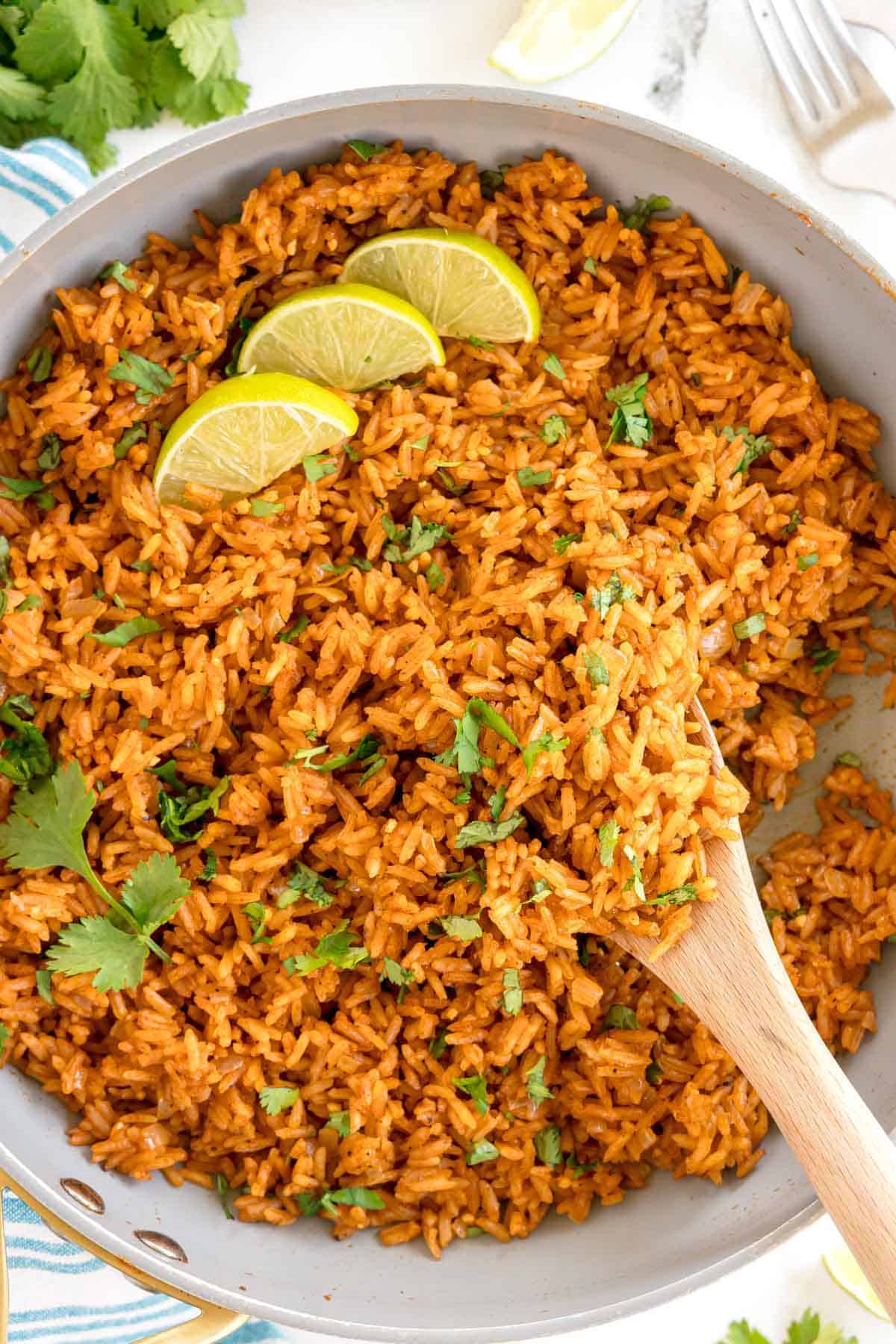 A skillet of cooked Spanish rice garnished with lime wedges and cilantro.