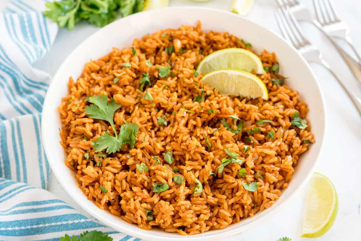 A white bowl filled with Spanish rice, topped with lime wedges and cilantro.