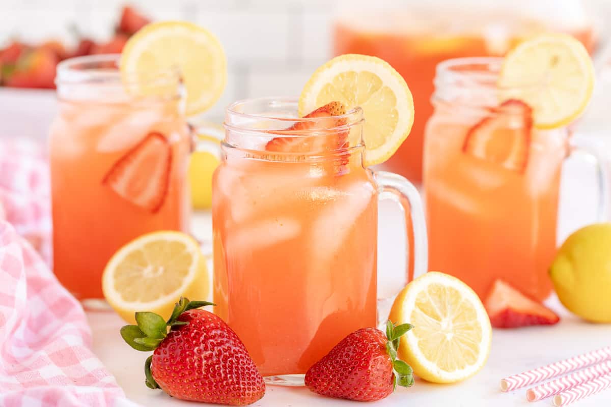 mason jar glasses of strawberry lemonade with strawberries and lemons on the side.